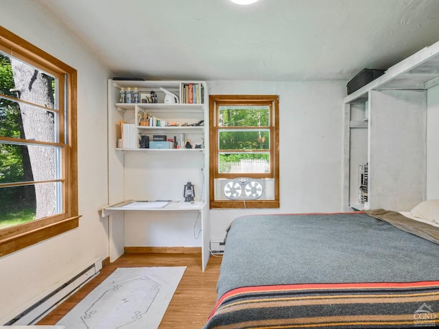 bedroom featuring hardwood / wood-style floors, multiple windows, and a baseboard heating unit