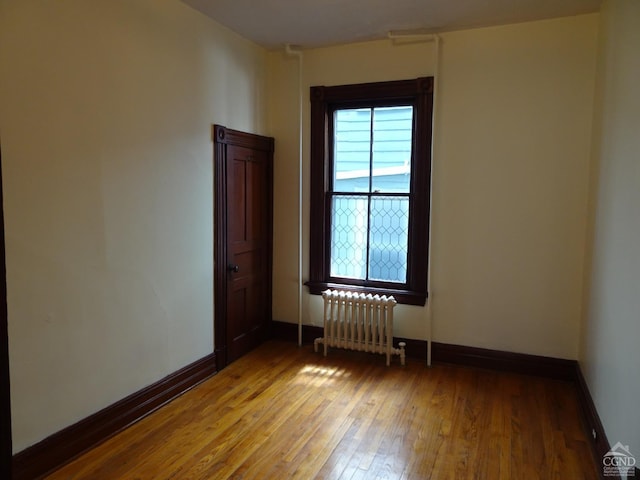 unfurnished room with radiator, baseboards, and light wood-style floors