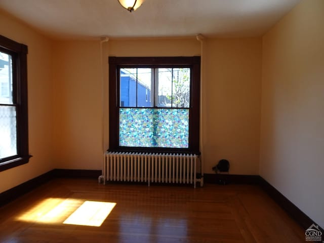 unfurnished room with radiator heating unit, a healthy amount of sunlight, wood finished floors, and baseboards