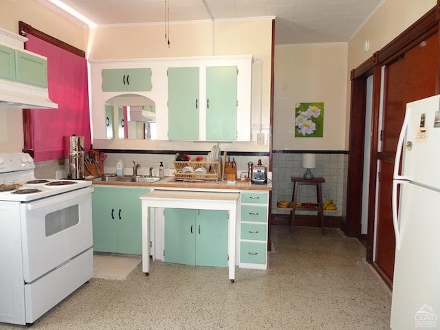 kitchen with a sink, a wainscoted wall, under cabinet range hood, ornamental molding, and white appliances