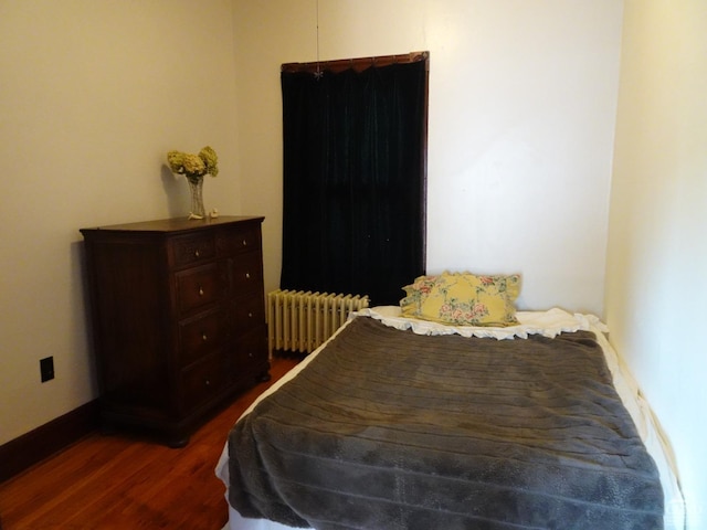 bedroom with radiator heating unit, wood finished floors, and baseboards