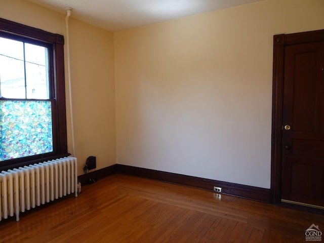 unfurnished room featuring baseboards, radiator, and wood finished floors