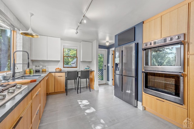 kitchen featuring appliances with stainless steel finishes, sink, light brown cabinets, white cabinets, and hanging light fixtures