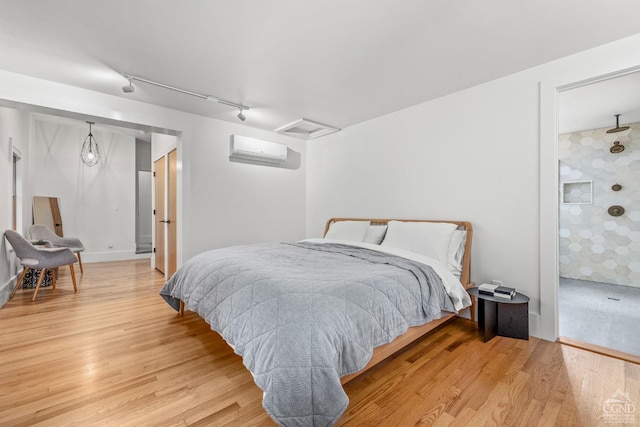 bedroom with a wall mounted air conditioner, wood-type flooring, and rail lighting