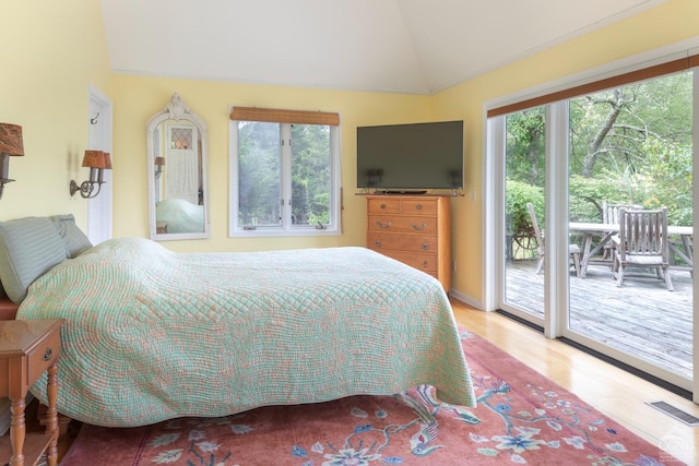 bedroom featuring vaulted ceiling, access to exterior, light hardwood / wood-style flooring, and multiple windows