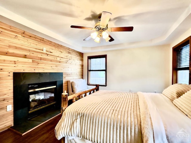 bedroom with a tile fireplace, hardwood / wood-style flooring, ceiling fan, and wooden walls