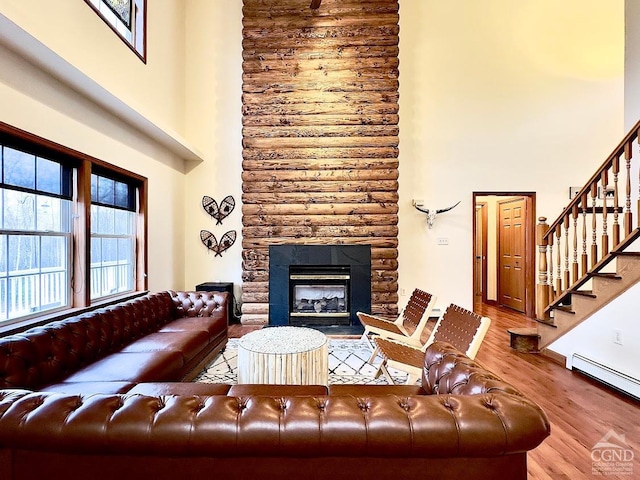 living room with a high ceiling, a fireplace, light hardwood / wood-style floors, and a baseboard radiator