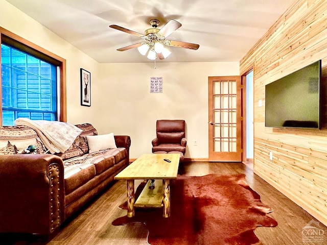 living room featuring wood-type flooring, ceiling fan, and wood walls