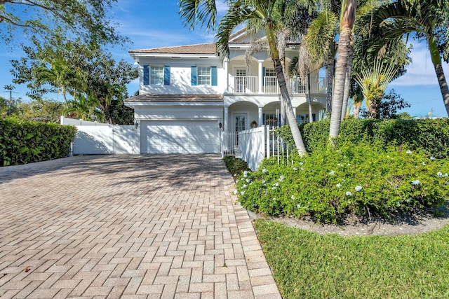 view of front facade with a balcony, a garage, fence, decorative driveway, and stucco siding