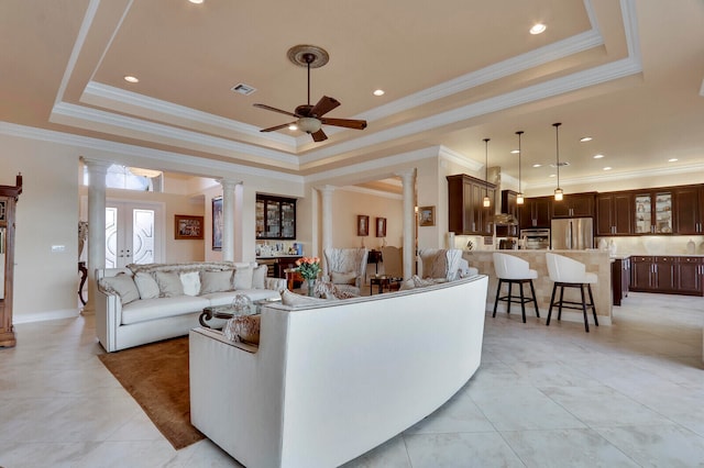 living room featuring ceiling fan, a raised ceiling, ornate columns, and crown molding