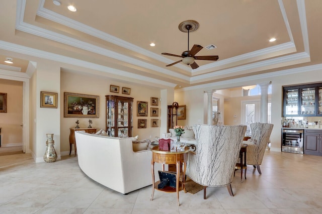 living room with decorative columns, crown molding, a tray ceiling, and beverage cooler