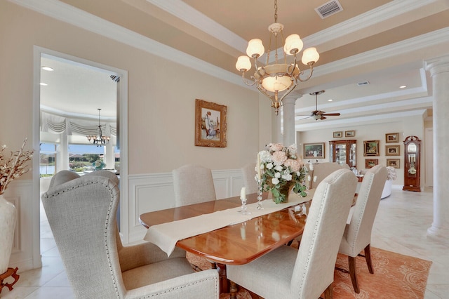 tiled dining space featuring ceiling fan with notable chandelier, ornamental molding, a tray ceiling, and decorative columns