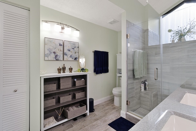 bathroom featuring vanity, toilet, a textured ceiling, an enclosed shower, and wood-type flooring