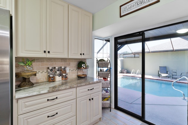 kitchen with stainless steel fridge, light wood-type flooring, light stone counters, and a healthy amount of sunlight