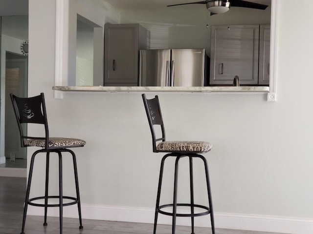 kitchen with a kitchen bar, stainless steel fridge, ceiling fan, gray cabinetry, and dark hardwood / wood-style floors