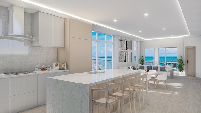 kitchen featuring sink, a center island with sink, a water view, and wall chimney exhaust hood