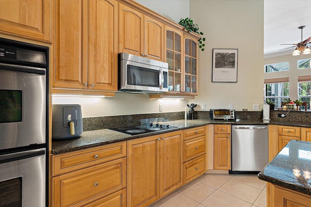 kitchen featuring light tile patterned flooring, ceiling fan, stainless steel appliances, and dark stone countertops