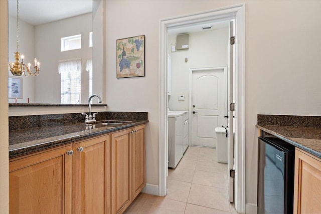 kitchen with light tile patterned flooring, sink, dark stone countertops, pendant lighting, and washing machine and dryer