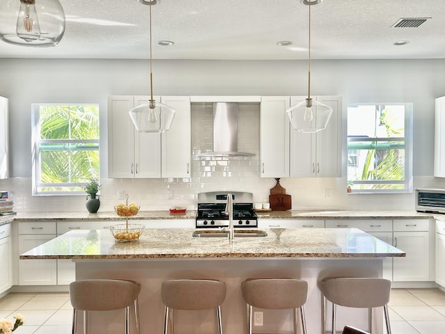 kitchen featuring white cabinets, wall chimney range hood, and gas range