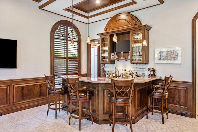 bar with wet bar, ornamental molding, decorative light fixtures, wainscoting, and a tray ceiling