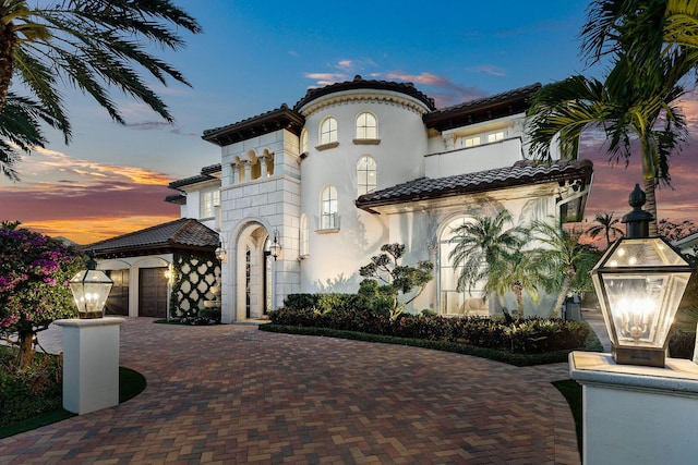 mediterranean / spanish-style house with a garage, stucco siding, decorative driveway, and a tile roof
