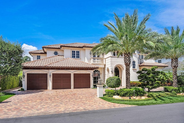 mediterranean / spanish-style house featuring a balcony, stucco siding, decorative driveway, a tile roof, and a garage