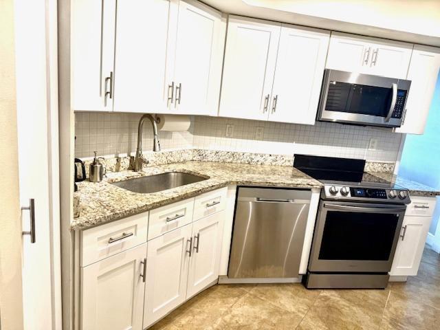 kitchen with white cabinetry, sink, light stone counters, and appliances with stainless steel finishes