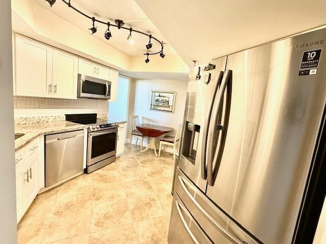 kitchen featuring light tile patterned flooring, tasteful backsplash, white cabinetry, light stone counters, and stainless steel appliances