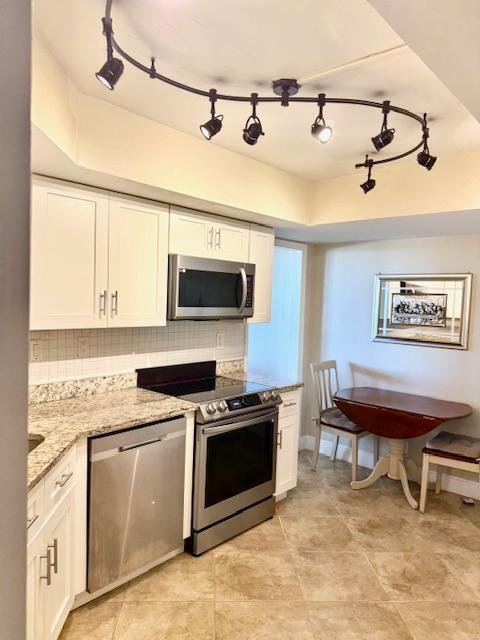 kitchen with backsplash, stainless steel appliances, white cabinets, and light stone countertops