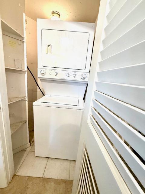 laundry room with stacked washing maching and dryer and light tile patterned floors