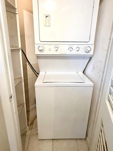 washroom with stacked washing maching and dryer, light tile patterned flooring, and tile walls