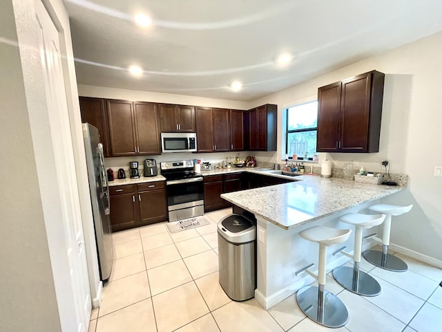 kitchen with stainless steel appliances, a sink, dark brown cabinetry, a peninsula, and a kitchen bar