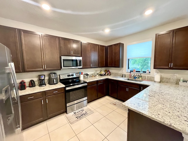 kitchen featuring light stone counters, light tile patterned floors, appliances with stainless steel finishes, a sink, and dark brown cabinetry