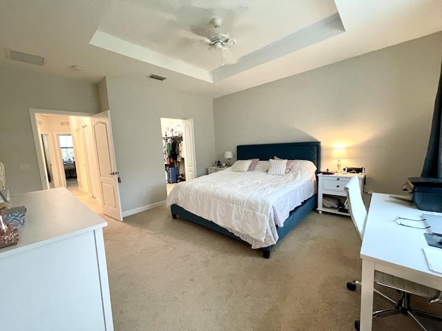 bedroom featuring a spacious closet, a raised ceiling, visible vents, and light colored carpet