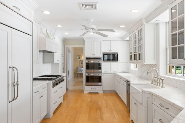 kitchen with crown molding, built in appliances, sink, white cabinets, and light hardwood / wood-style flooring