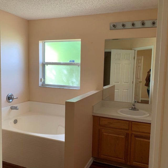 bathroom with a textured ceiling, vanity, and tiled tub