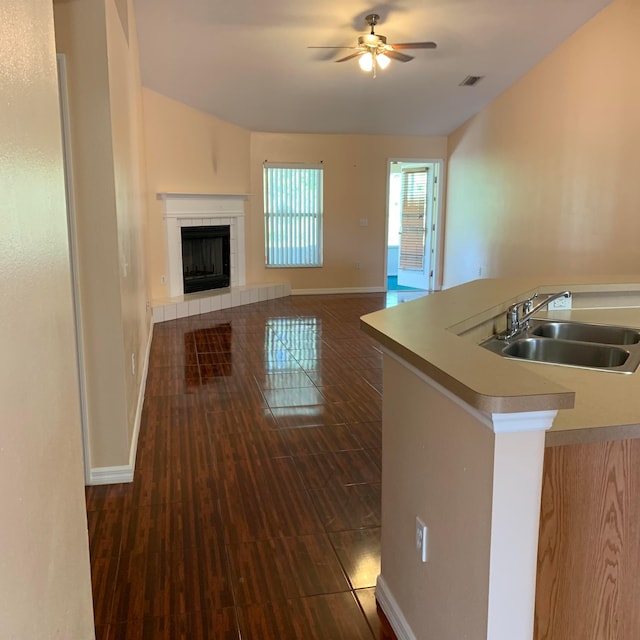 kitchen featuring dark hardwood / wood-style floors, ceiling fan, sink, and a tile fireplace