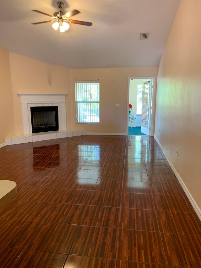 unfurnished living room with a tiled fireplace, lofted ceiling, dark wood-type flooring, and ceiling fan