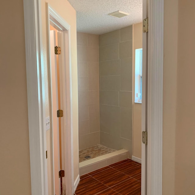 bathroom featuring a tile shower, a textured ceiling, and tile floors