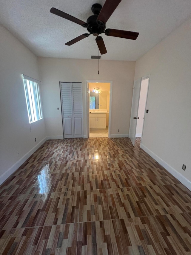 unfurnished bedroom featuring a textured ceiling, dark wood-type flooring, a closet, ceiling fan, and connected bathroom