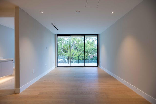 empty room with floor to ceiling windows and light wood-type flooring