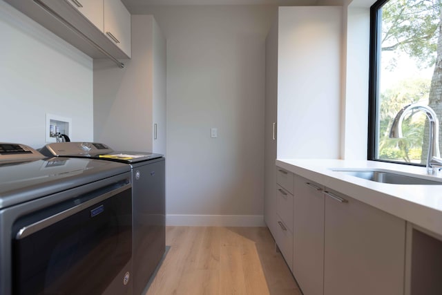 laundry room with sink, a healthy amount of sunlight, cabinets, washing machine and dryer, and light wood-type flooring