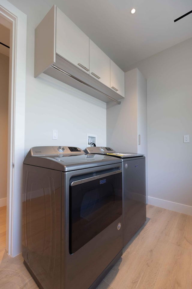 laundry area featuring cabinets, washer and dryer, hookup for a washing machine, and light hardwood / wood-style flooring