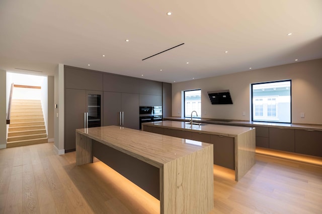 kitchen with double oven, light hardwood / wood-style floors, a center island with sink, gray cabinets, and sink