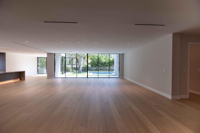 empty room with floor to ceiling windows and light hardwood / wood-style flooring