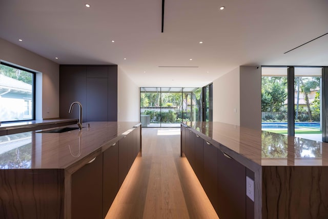 kitchen featuring light wood-type flooring, a large island with sink, a wall of windows, dark stone countertops, and sink