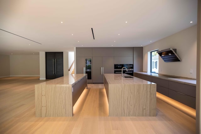 kitchen with light hardwood / wood-style floors, a kitchen island with sink, and gray cabinets