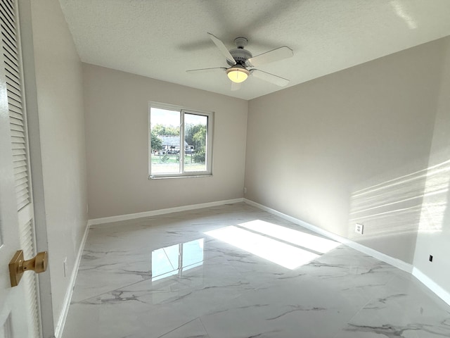 unfurnished room with marble finish floor, a textured ceiling, and baseboards