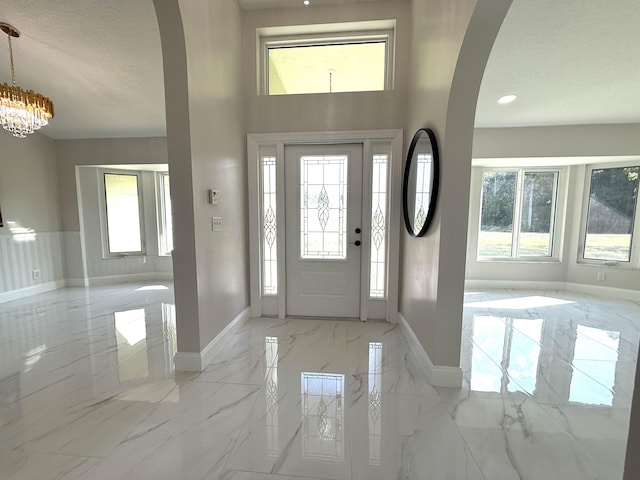 entrance foyer with marble finish floor, recessed lighting, arched walkways, baseboards, and a chandelier