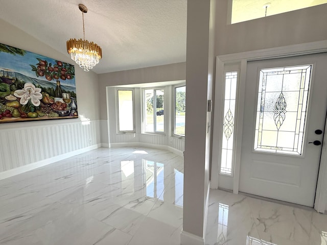 foyer entrance featuring a wainscoted wall, marble finish floor, a textured ceiling, an inviting chandelier, and baseboards